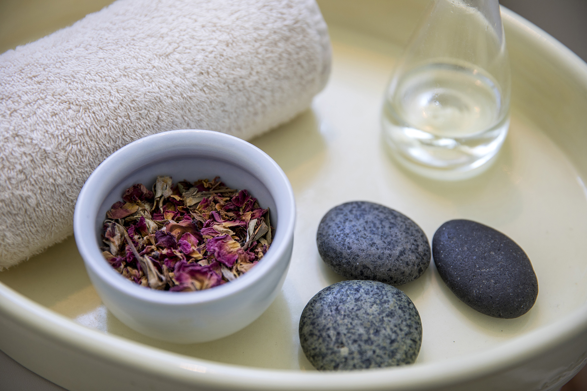 A tray in spa filled with a towel, potpourri, hot stones and a glass of water.